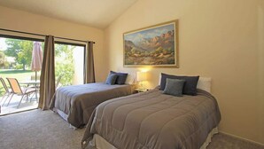 A hotel room with two beds, a painting of a landscape, a table with chairs, and a view of the outdoors. - Condo with views, BBQ|Pool, golf, tennis access (Palm Desert)