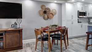 Une cuisine moderne avec des meubles blancs, un four à micro-ondes encastré et un coin repas comprenant une table et des chaises en bois.