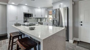 Une cuisine moderne avec des meubles blancs, un réfrigérateur en acier inoxydable et un îlot en marbre agrémenté de tabourets.