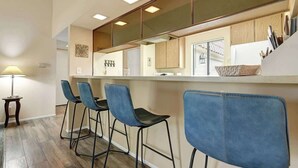 Een moderne keuken met een bar, houten kasten en blauwe barkrukken.