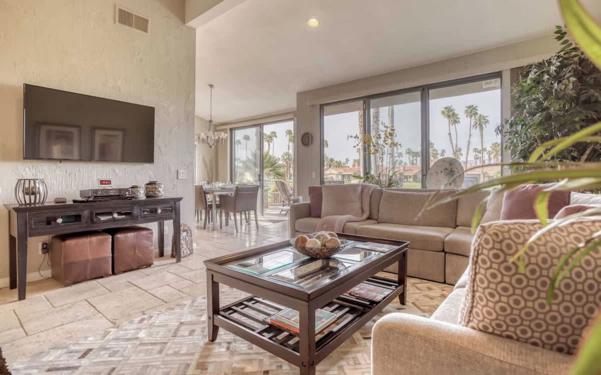 Settle into your bright, open living space where floor-to-ceiling windows frame swaying palm trees and sunshine spills across plush seating—your perfect spot to unwind after exploring the area.
