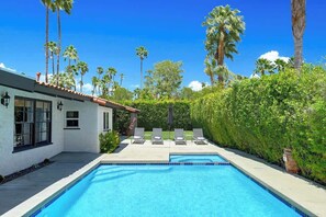 A swimming pool with lounge chairs and a white building with windows and a tiled roof. - Centrally located and pet-friendly home with pool (Palm Springs)