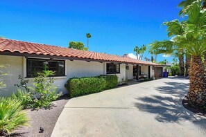 A two-story building with a red-tiled roof, a concrete driveway, and a well-maintained garden with various plants and a palm tree. - Centrally located and pet-friendly home with pool (Palm Springs)