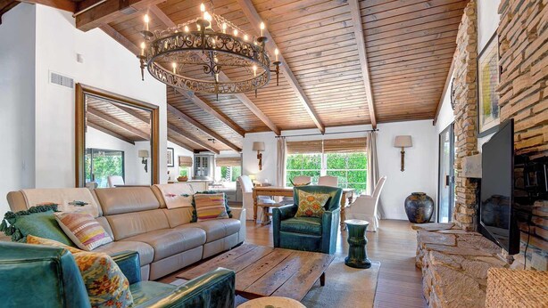 A spacious living room with a leather sofa, a teal armchair, a wooden coffee table, a stone fireplace, and a chandelier. - Centrally located and pet-friendly home with pool (Palm Springs)