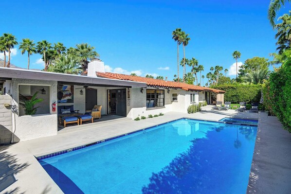 A poolside area with a clear blue pool, outdoor seating, and palm trees. - Centrally located and pet-friendly home with pool (Palm Springs)