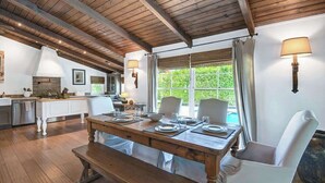 A dining area with a wooden table set for four, white chairs, a bench, and a view of greenery outside. - Centrally located and pet-friendly home with pool (Palm Springs)
