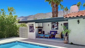 A poolside area with a built-in fireplace, outdoor seating, and a view of mountains. - Centrally located and pet-friendly home with pool (Palm Springs)