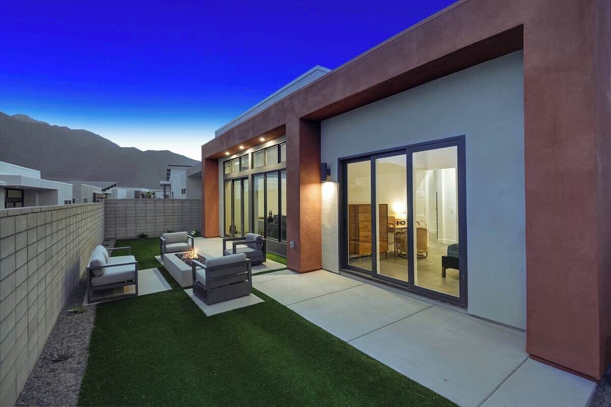 Une maison moderne dotée d’un patio, d’un foyer extérieur et d’une grande porte-fenêtre coulissante donnant sur l’intérieur.
