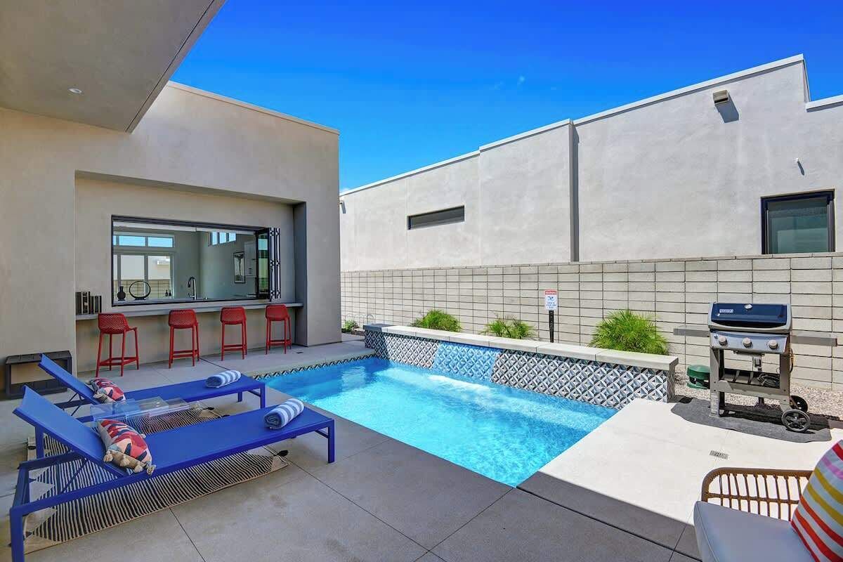 A modern outdoor pool area with lounge chairs and a barbecue grill.