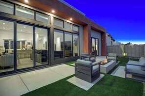 A modern house with a spacious patio, a fire pit, and a well-lit interior. - Pet-friendly home with heated spool + fire pit (Palm Springs)