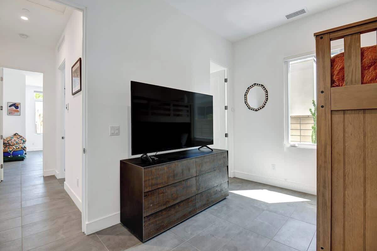 Una sala moderna con un televisor de pantalla plana grande sobre un mueble de madera oscura, paredes blancas y una puerta de madera.