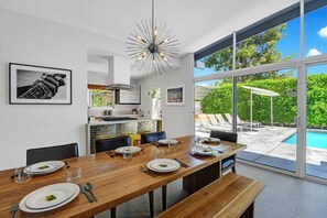 A modern dining area with a wooden table, chairs, and a view of a swimming pool. - Dog-Friendly Stunner|Pool|Fireplace|BBQ and more (Palm Springs)