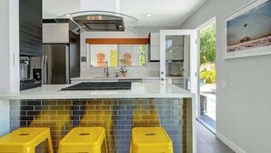 Une cuisine moderne dotée d’un grand îlot central, de tabourets jaunes et offrant une vue sur l’extérieur.