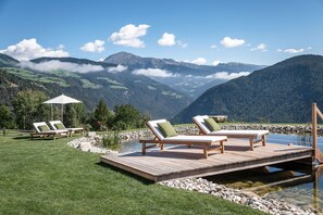 Um deck de madeira com cadeiras de descanso com vista para um lago montanhoso.