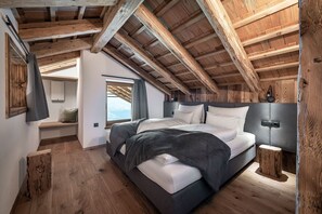 Quarto com teto de madeira, cama com roupa de cama branca, mesa de cabeceira e janela com vista.