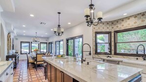 A modern kitchen with a large island, pendant lighting, and large windows offering views of greenery. - Pet-friendly tennis estate in The Mesa|360-views (Palm Springs)