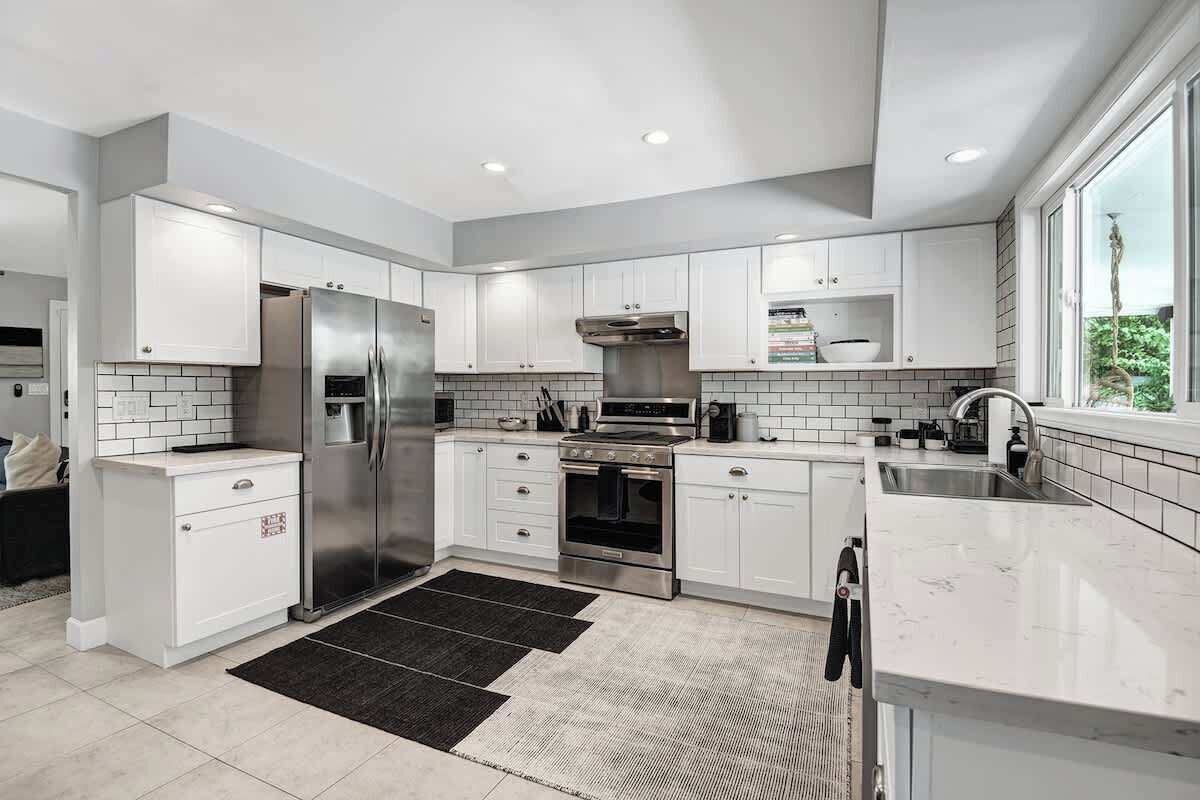 A modern kitchen with white cabinetry, stainless steel appliances, and a black rug.