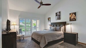 Ein Schlafzimmer mit Bett, Schreibtisch, Stuhl, Deckenventilator und einem Fenster mit Jalousien.