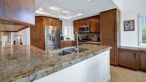 Eine moderne Küche mit Granitarbeitsplatten, Edelstahlgeräten, Holzschränken und einem Deckenventilator.