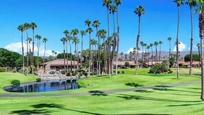 A golf course with a pond, palm trees, and buildings in the background. - Condo with Golf Course Views (Palm Desert)