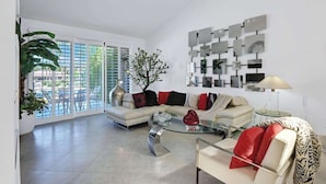 A modern living room with a sofa, coffee table, and a wall-mounted art display. - Condo with Golf Course Views (Palm Desert)