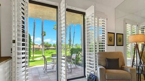 Habitación con puerta de vidrio corredera que da a un patio con vista a palmeras y un campo de golf.