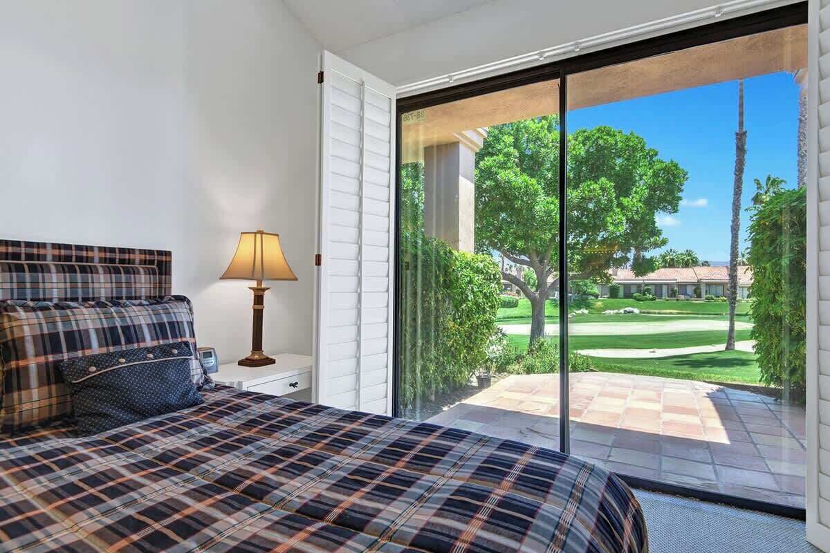 Une chambre avec un lit, une lampe et une vue sur un terrain de golf, visible à travers une porte-fenêtre coulissante.