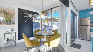 A modern kitchen with a dining area, featuring a round table with chairs, a chandelier, and a large window offering a view of the outdoors. - Retro Mid-Century Modern Retreat at Historic Ocotillo Lodge (Palm Springs)