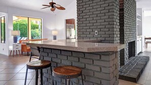Eine Küche mit Kamin aus Ziegelsteinen, einer Bar mit Hockern und einem Deckenventilator.