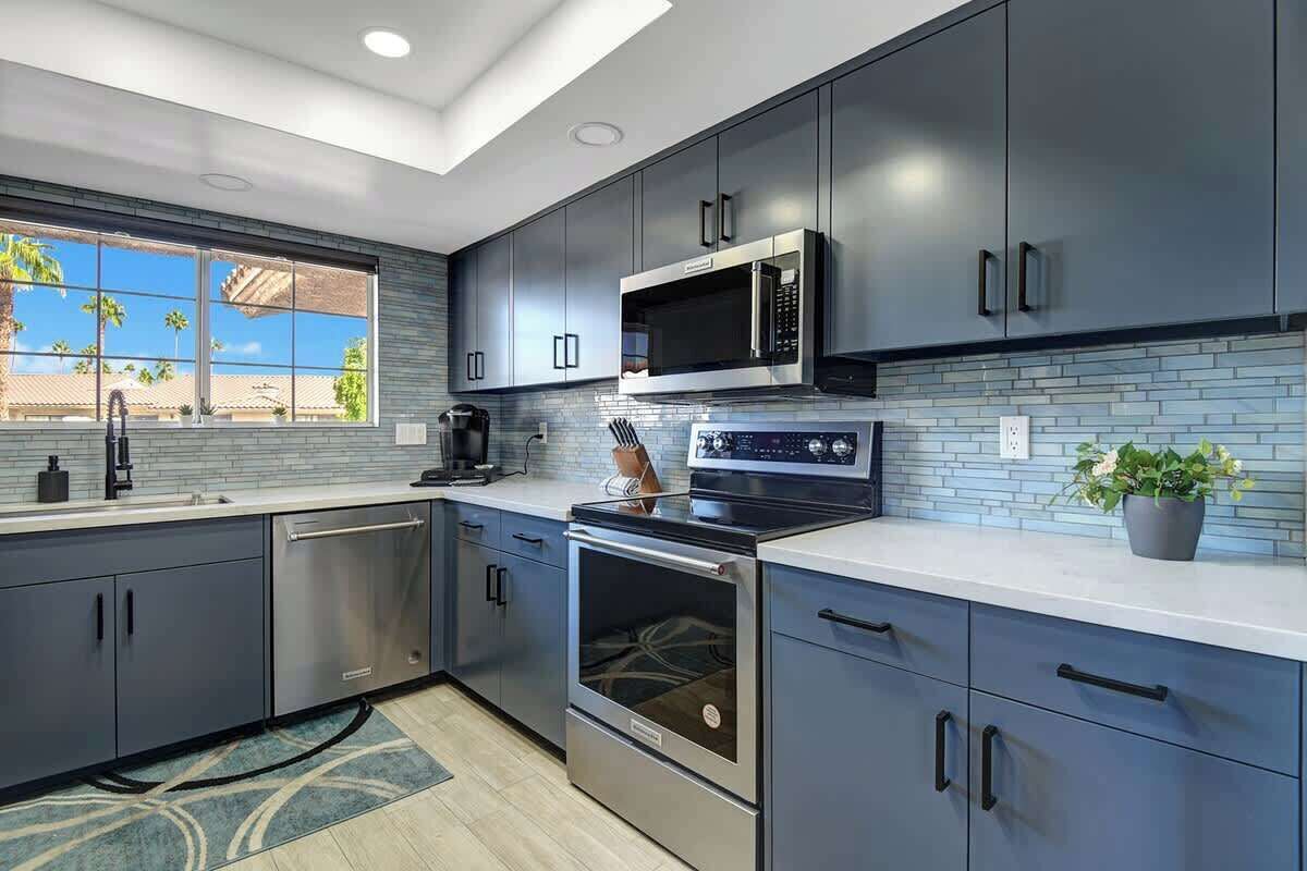 A modern kitchen with dark cabinets, stainless steel appliances, and a window with a view of palm trees.