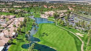 Ein Golfplatz mit mehreren Wasserhindernissen, umgeben von Palmen und Wohnhäusern.