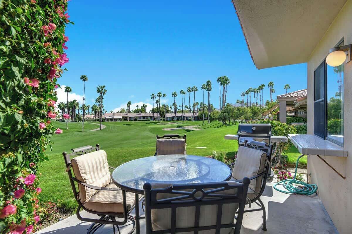 An outdoor patio with a round glass table and chairs, overlooking a well-manicured lawn and golf course.