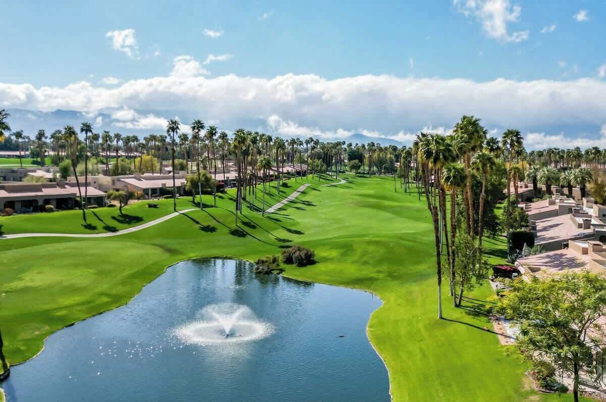 A golf course with a pond, palm trees, and buildings in the background.