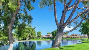 Un parcours de golf avec un étang, de grands arbres et un bâtiment en arrière-plan.