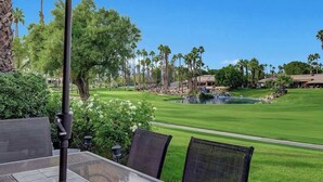 Un parcours de golf offrant une vue sur un étang, des palmiers et un bâtiment en arrière-plan.