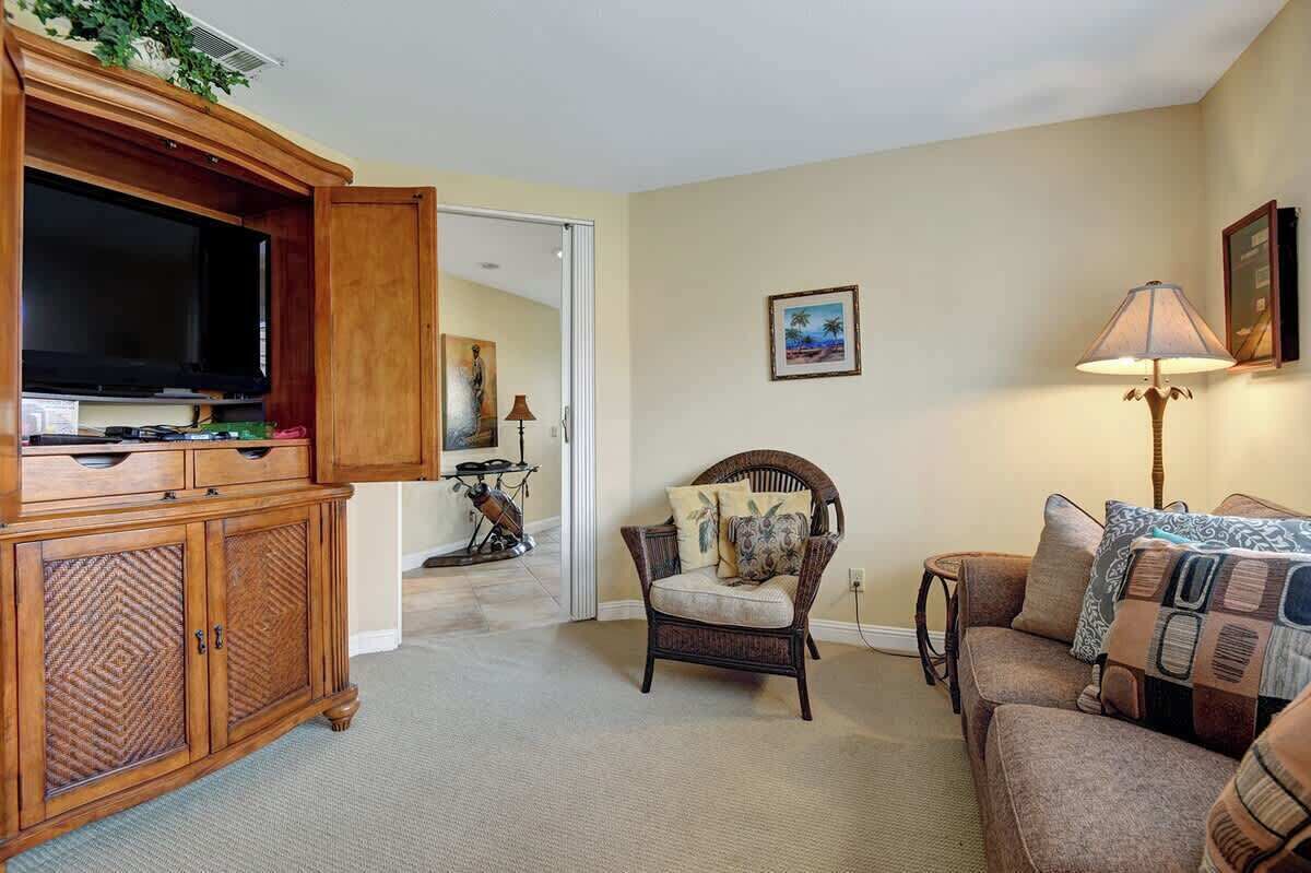 A living room with a wooden entertainment center, a television, a wicker armchair, a sofa, and a lamp.