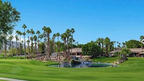 Un terrain de golf avec un étang, des palmiers et des bâtiments en arrière-plan.