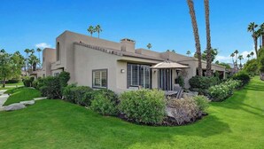 Une maison moderne dotée d’une pelouse bien entretenue, de palmiers et d’un espace patio.