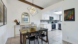 A modern kitchen with white cabinets, a microwave, and a dining area with a glass table and chairs. - Pet Friendly Bungalow in Mesquite Country Club (Palm Springs)