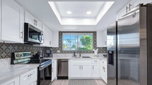 A modern kitchen with white cabinets, stainless steel appliances, a large window with a view, and a skylight. - Pet Friendly Bungalow in Mesquite Country Club (Palm Springs)