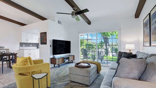 A modern living room with a sofa, armchair, and ottoman, a flat-screen TV, and a dining area with a table and chairs. - Pet Friendly Bungalow in Mesquite Country Club (Palm Springs)