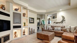 A spacious living room with a large sectional sofa, leather ottoman, and a flat-screen TV mounted on the wall. - Spacious Condo|Great Views|Platinum Membership (Palm Desert)