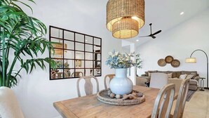 A dining area with a wooden table, chairs, a vase with flowers, a woven placemat, a hanging light fixture, a ceiling fan, a wall-mounted mirror, and a sofa in the background. - Pet Friendly|2 Suites+ guest room|Large Patio|Fairway Views (Palm Desert)