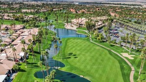A golf course with a pond, palm trees, and a view of a cityscape in the background. - Pet Friendly|2 Suites+ guest room|Large Patio|Fairway Views (Palm Desert)