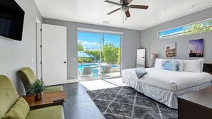 A modern bedroom with a large bed, a ceiling fan, a TV mounted on the wall, and a view of a swimming pool through the glass door. - Pet-friendly Desert Park home with heated pool|Spa (Palm Springs)