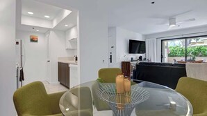 Een moderne woonkamer met een glazen salontafel, groene fauteuils, een flatscreen televisie en uitzicht op het omliggende landschap.