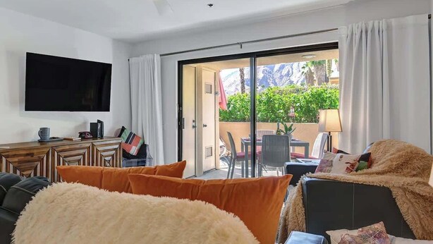 Een moderne woonkamer met een flatscreen televisie, een houten dressoir en een schuifpui die leidt naar een terras.