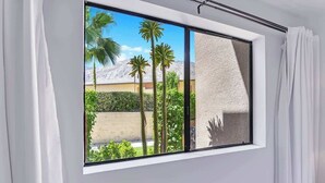 Een kamer met een groot raam en uitzicht op palmbomen en een berg.