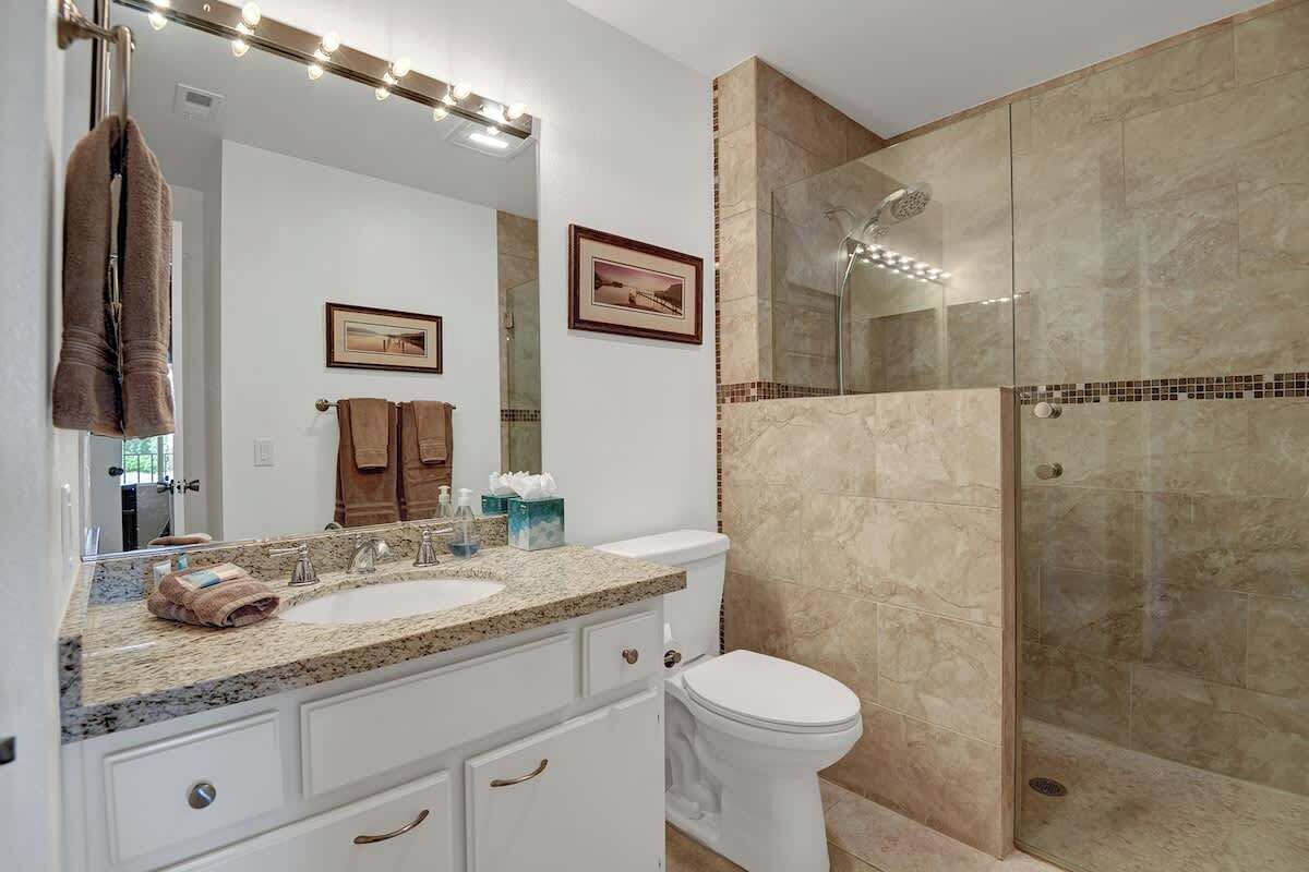 A bathroom with a vanity, two sinks, a toilet, and a glass-enclosed shower.