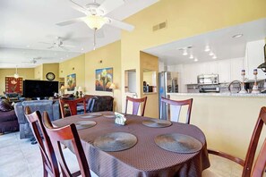 A dining area with a table set for four, a kitchen in the background, and a living room with a sofa and TV. - PGA West Condo with Views (La Quinta)